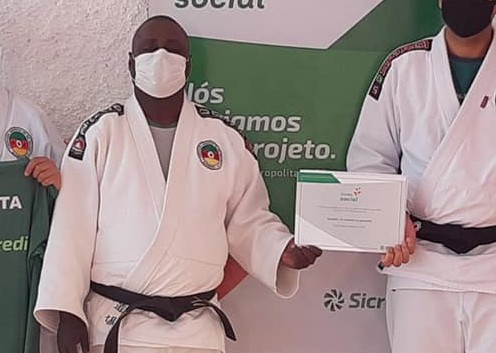 Descrição da imagem: Foto do sansei Jorge Henrique vestindo o seu Judogi branco com a faixa preta. Ele está segurando um certificado nas mãos. Fim da descrição