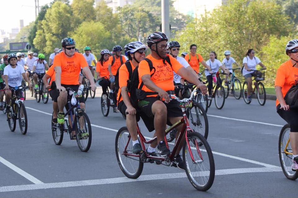 Descrição da imagem: foto em orientação paisagem destacando os ciclistas em bicicletas de dois lugares. Eles usam camiseta laranja do grupo pedal da ACERGS. Fim da descrição.