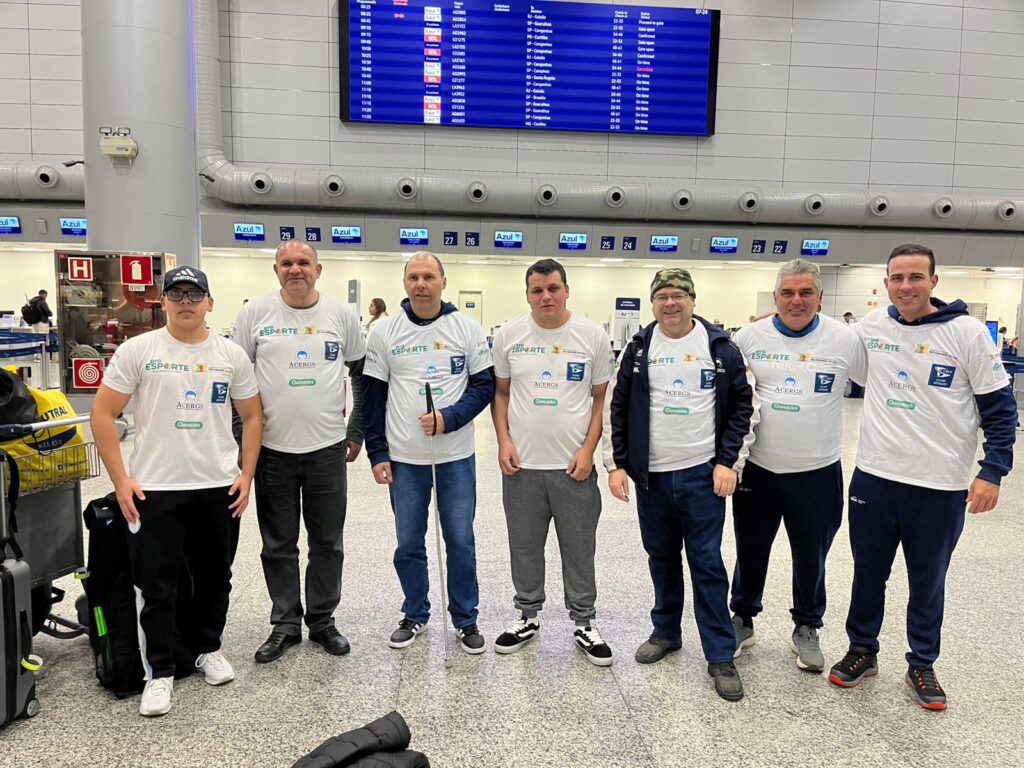 Delegação na área de embarque do aeroporto, usando camisetas brancas personalizadas com logo dos apoiadores.

Da esquerda para a direita estão: Galo, Edinei, Glailton, Lucas, Aurélio, Anderson e Natan.